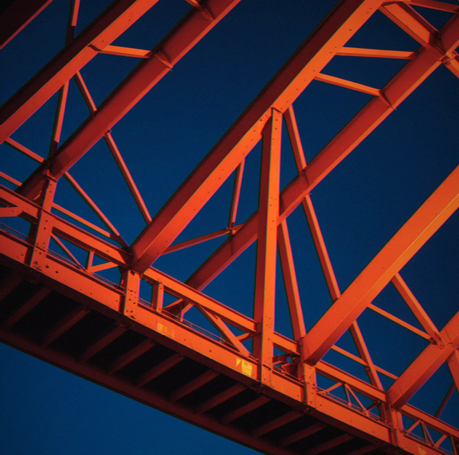 Steel truss joint bent at a tight angle under straight-line load. The sharp corner glows red where stress peaks, fading to orange as it spreads outward